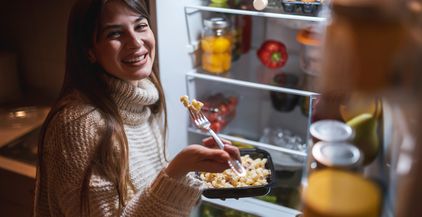woman-eating-pasta-next-to-an-opened-fridge-door-a-2021-12-09-09-36-26-utc