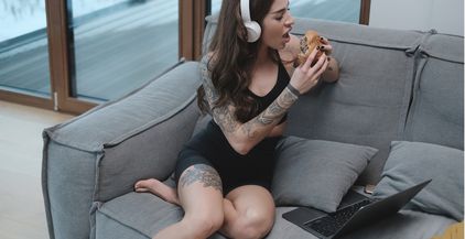 tattooed-woman-eats-burger-sitting-on-sofa-with-he-2021-08-30-18-58-40-utc